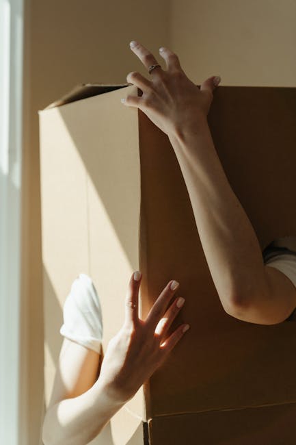 Close-up view of three brown cardboard moving boxes stacked inside a property, with the top box marked 'STUFF' in red marker and a small smiley face drawn underneath, and the bottom box labeled 'CLOTH